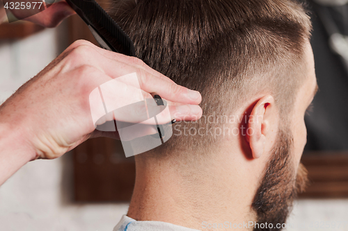 Image of The hands of barber making haircut to young man in barbershop