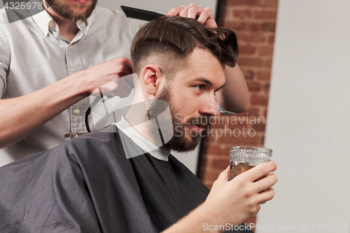 Image of Young handsome barber making haircut of attractive man in barbershop