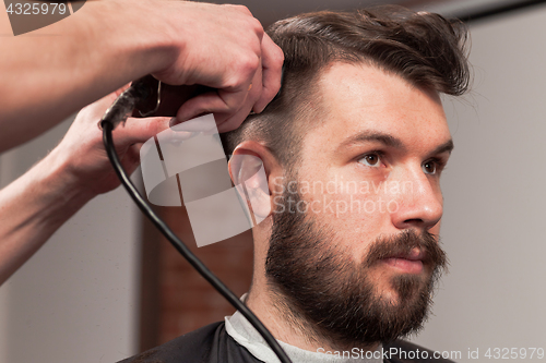 Image of The hands of barber making haircut to young man in barbershop