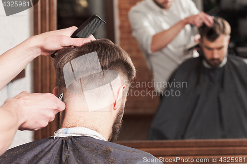 Image of The hands of barber making haircut to young man in barbershop