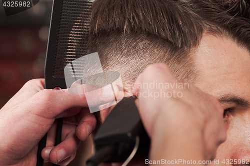 Image of The hands of barber making haircut to young man in barbershop