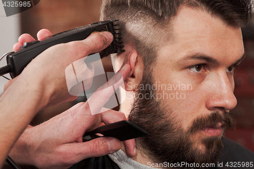 Image of The hands of barber making haircut to young man in barbershop