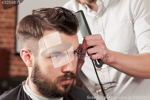 Image of The hands of barber making haircut to young man in barbershop