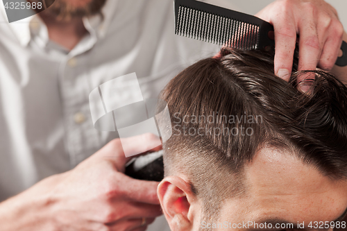 Image of The hands of barber making haircut to young man in barbershop