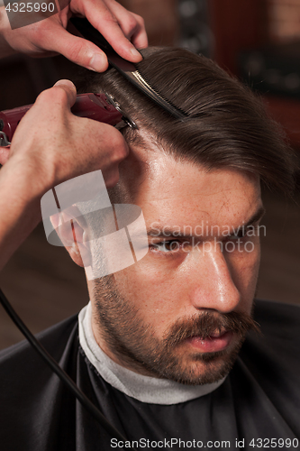 Image of The hands of barber making haircut to young man in barbershop