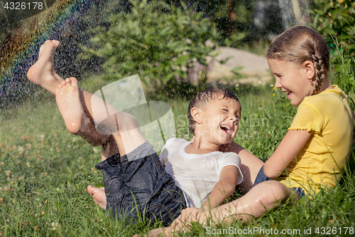 Image of Happy kids sitting on the grass and pouring water from a hose.