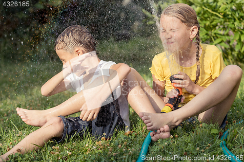 Image of Happy kids sitting on the grass and pouring water from a hose.