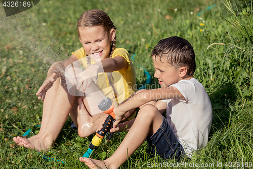 Image of Happy kids sitting on the grass and pouring water from a hose.