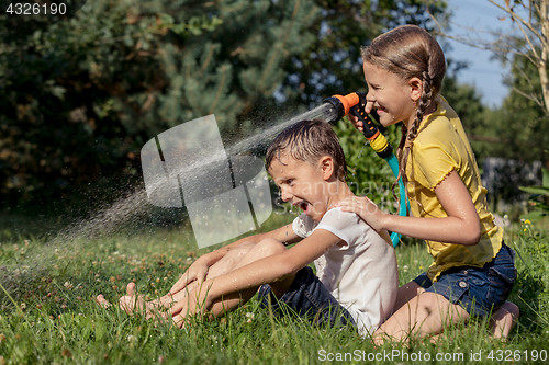 Image of Happy kids sitting on the grass and pouring water from a hose.