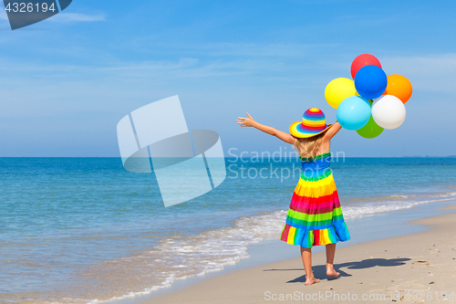 Image of Little girl with balloons standing on the beach 