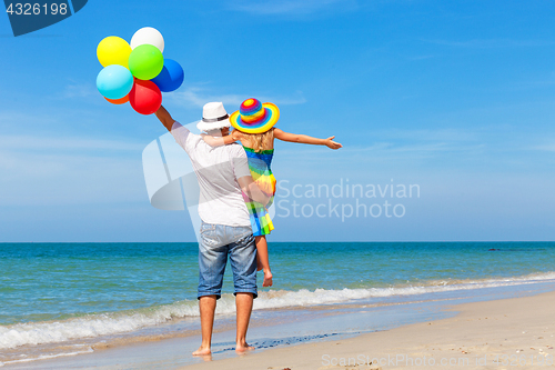 Image of Father and daughter with balloons playing on the beach at the da