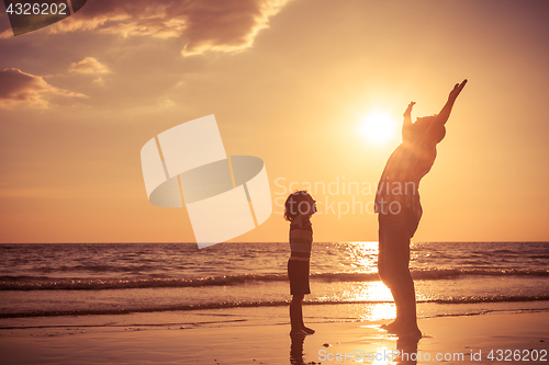 Image of Father and son playing on the beach at the sunset time. 