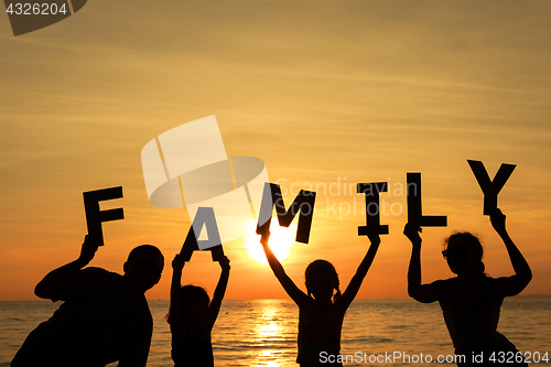 Image of Happy family standing on the beach at the sunset time.