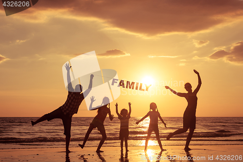 Image of Happy family standing on the beach at the sunset time.
