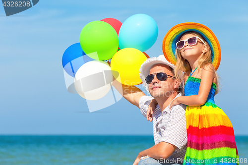 Image of Father and daughter with balloons playing on the beach at the da