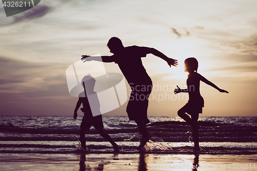 Image of Father and children playing on the beach at the sunset time. 