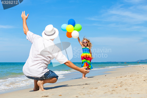 Image of Father and daughter with balloons playing on the beach at the da