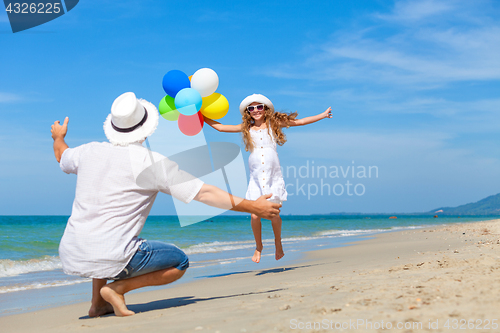 Image of Father and daughter with balloons playing on the beach at the da