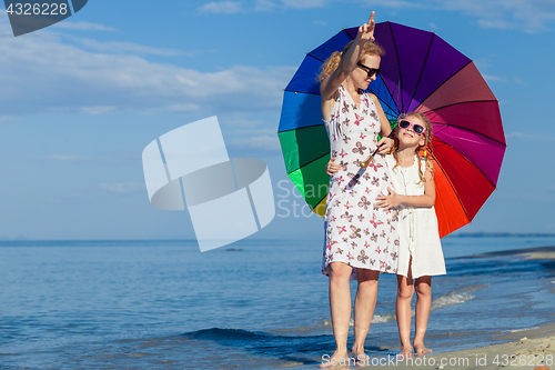 Image of Mother and daughter playing with umbrella on the beach at the da