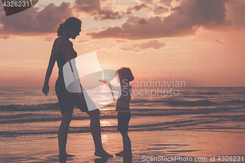 Image of Mother and son playing on the beach at the sunset time.