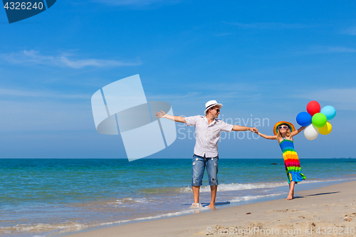 Image of Father and daughter with balloons playing on the beach at the da