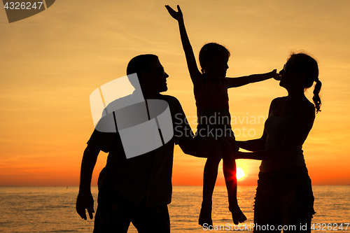 Image of Happy family standing on the beach at the sunset time.