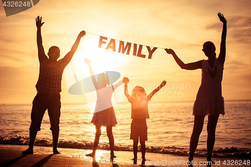 Image of Happy family standing on the beach at the sunset time.