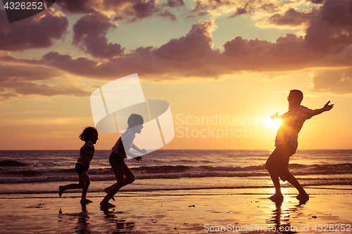 Image of Father and children playing on the beach at the sunset time.