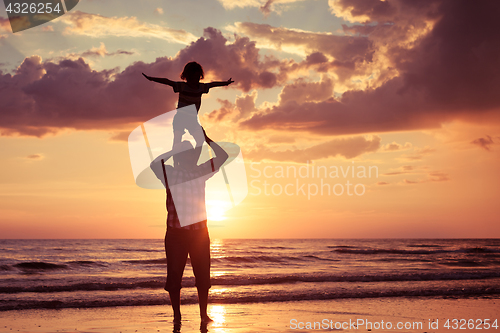 Image of Father and son playing on the beach at the sunset time.