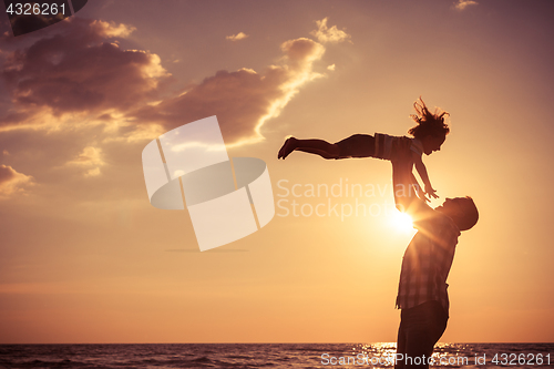 Image of Father and son playing on the beach at the sunset time.