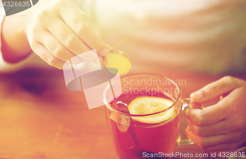 Image of close up of woman adding ginger to tea with lemon