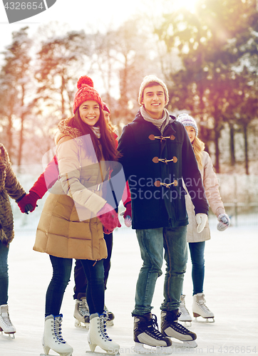 Image of happy friends ice skating on rink outdoors