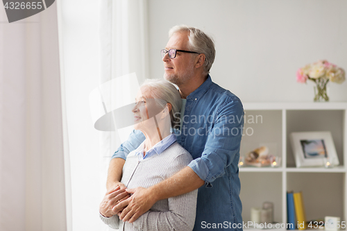 Image of happy senior couple looking through window at home