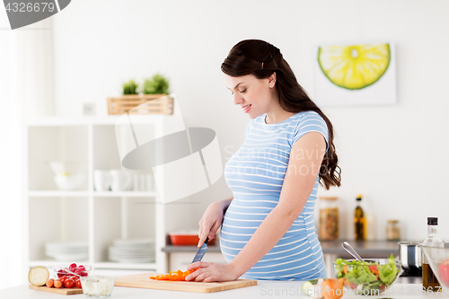 Image of pregnant woman cooking vegetable salad at home