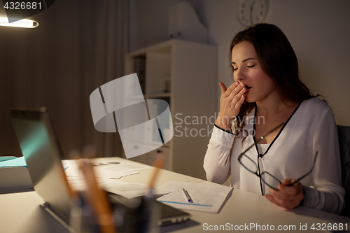 Image of tired woman with papers yawning at night office