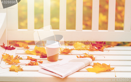 Image of newspaper and coffee cup on bench in autumn park