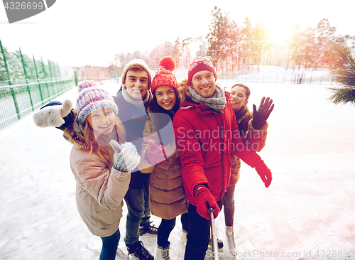 Image of happy friends with smartphone on ice skating rink