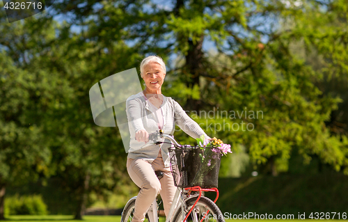 Image of happy senior woman riding bicycle at summer park