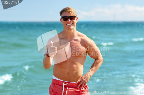 Image of smiling man showing thumbs up on summer beach