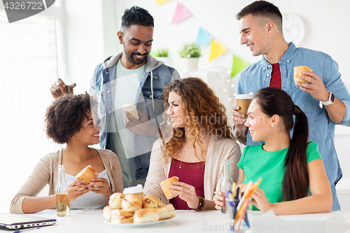 Image of happy friends or team eating at office party