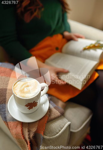 Image of Cup of cappuccino and girl reading a book