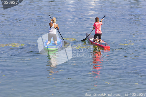 Image of Two women practicing paddle surf in lake