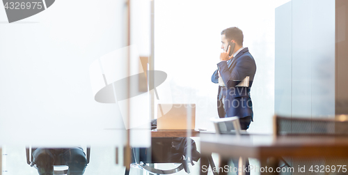 Image of Businessman talking on a mobile phone while looking through window.