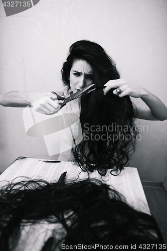 Image of beauty girl cuting her hair in empty fearing room with cutted hair, halloween creepy celebration art