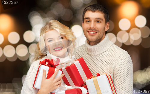 Image of happy couple in sweaters holding christmas gifts