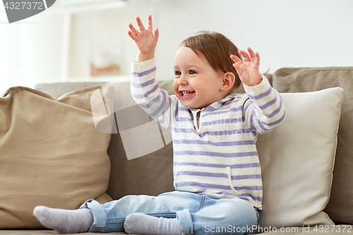 Image of happy smiling baby girl sitting on sofa at home