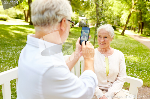 Image of old man photographing woman by smartphone in park