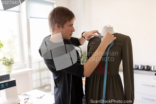 Image of fashion designer with dummy making dress at studio