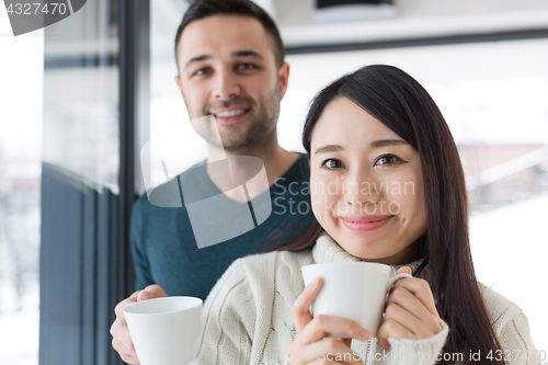 Image of multiethnic couple enjoying morning coffee by the window