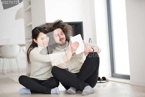 Image of multiethnic couple using tablet computer in front of fireplace